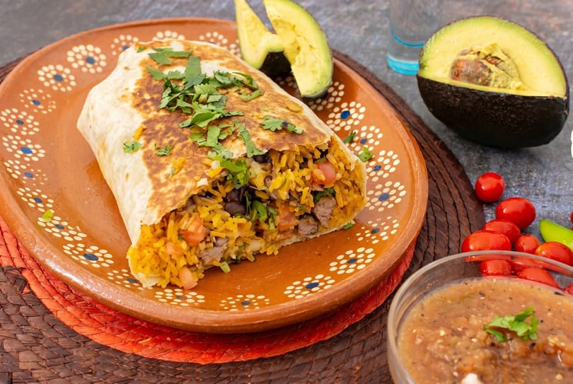 A large burrito filled with rice, beans, and meat, garnished with cilantro, on a decorative plate.