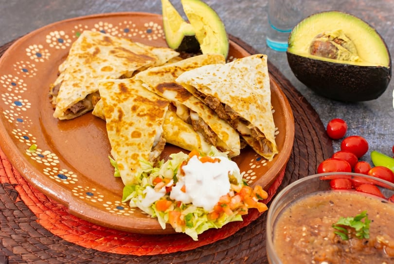 Beef quesadillas with sour cream, pico de gallo, and salsa on a decorative plate.