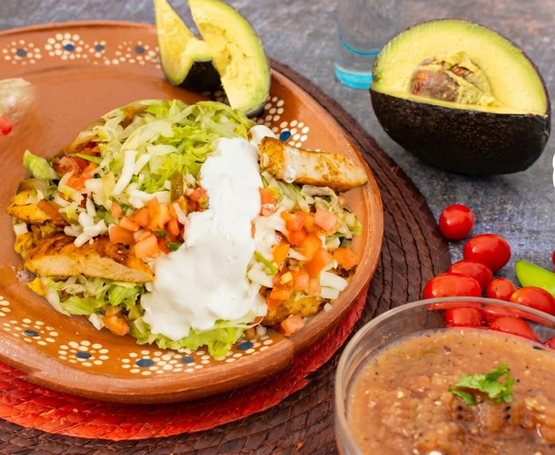 Chicken tacos with lettuce, pico de gallo, and sour cream, served with avocado and salsa.